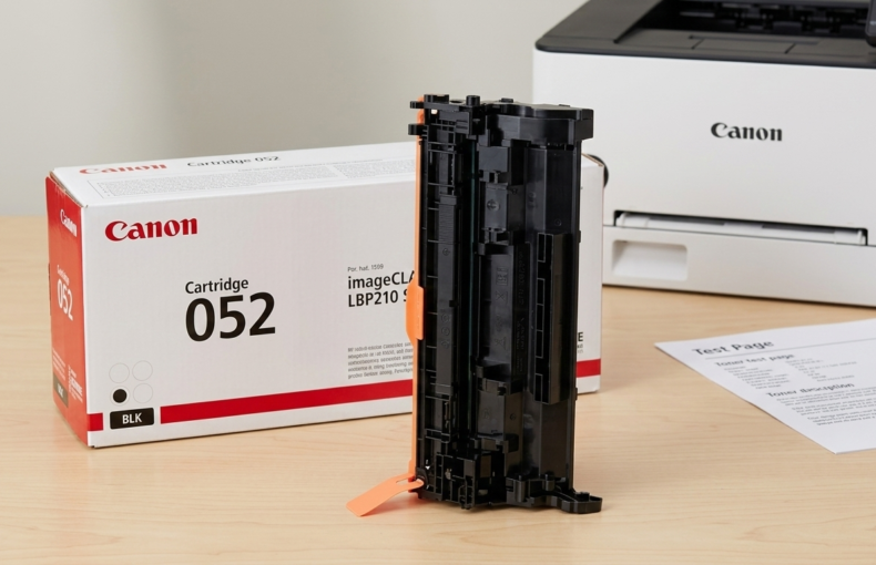Canon Cartridge 052 black toner box beside the cartridge and a printed test page, with a Canon printer in the background